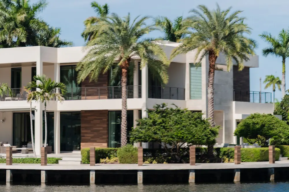 Modern two-story home with tall glass doors and royal palms along the water