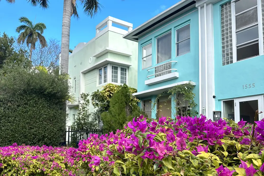 Pastel two-story homes behind bright pink bougainvillea and palm trees